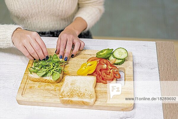 Unbekannte Person  die in der Küche zu Hause ein Gemüsesandwich zubereitet. Platzieren des Rucola