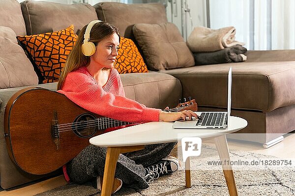 Frau lernt Gitarre spielen zu Hause mit Online-Unterricht am Computer