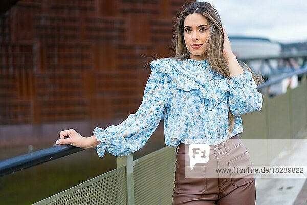 Junge Frau auf einer Brücke über einen Stadtfluss  lächelnd  Lifestyle-Konzept  blaues Hemd und braune Hose