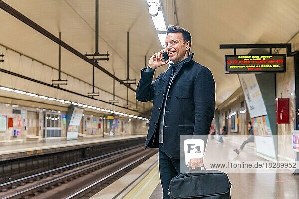 Kaukasischer Geschäftsmann mittleren Alters  der in der U-Bahn auf den Zug zur Arbeit wartet und dabei telefoniert
