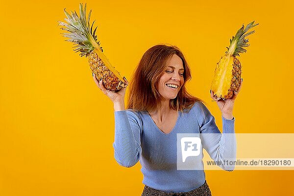 Frau mit Ananas und Sonnenbrille  tanzend und glücklich mit der halbierten Ananas  gelber Hintergrund