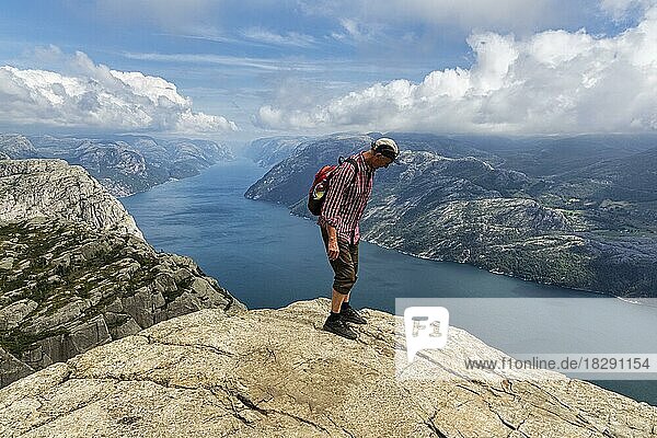 Hiker standing carefully at the rocky outcrop  view from the rocky outcrop Preikestolen to Lysefjord and mountains  sunny weather  Ryfylke  Rogaland  Norway  Europe