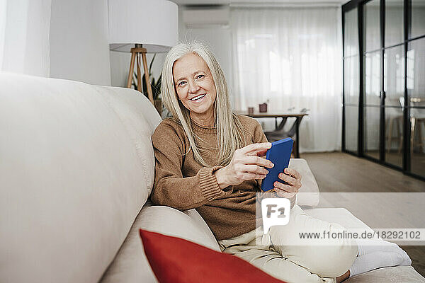 Happy mature woman sitting with mobile phone at home