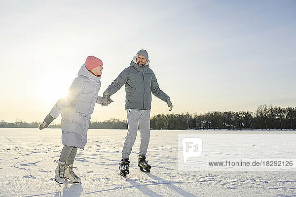Happy daughter with father practicing ice skating on winter lake