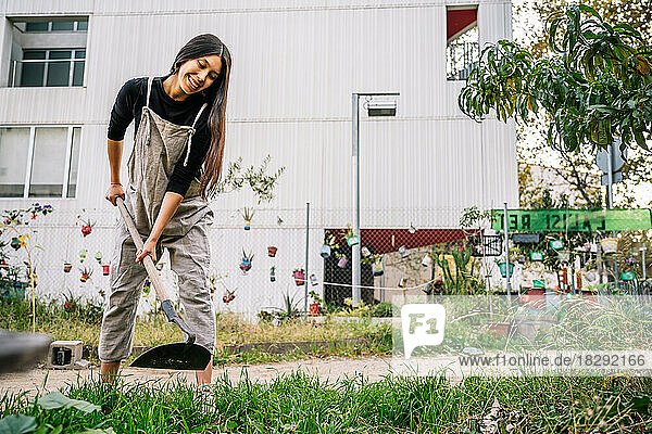 Happy young woman gardening with shovel in urban garden