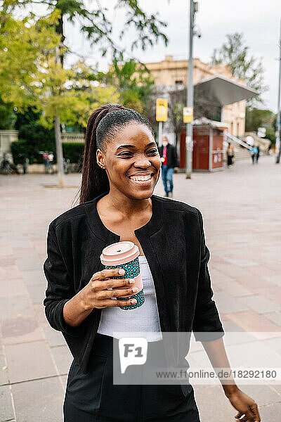 Happy businesswoman holding disposable cup on footpath