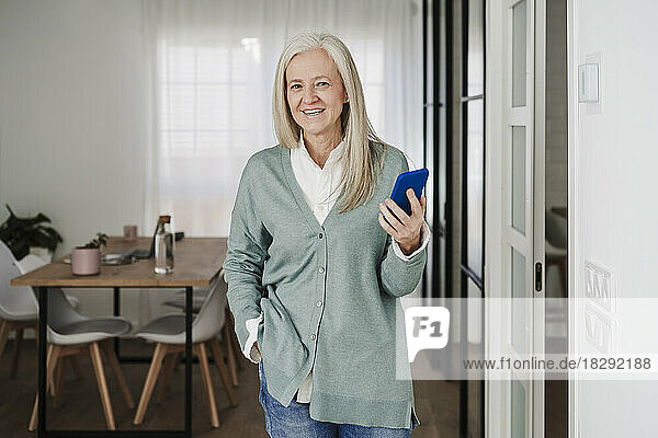 Smiling mature woman with smart phone standing at home