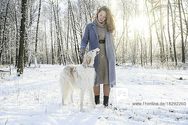 Mature woman standing with greyhound dog on snow in forest