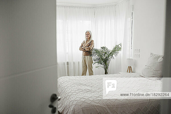 Mature woman with arms crossed standing in bedroom