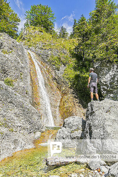 Germany  Bavaria  Male tourist standing on top of boulder lying in front of Rappinbach waterfall