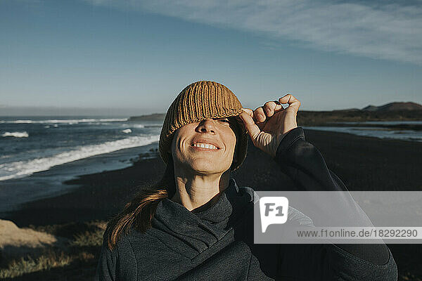 Smiling woman peeking through knit hat at Janubio Beach  Lanzarote  Canary Islands  Spain