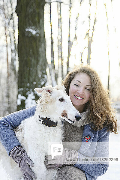 Happy mature woman with white greyhound dog in winter park