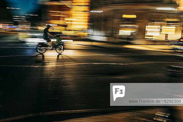 UK  England  London  Blurred motion of person riding motorcycle along city street at night