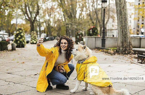 Glückliche junge Frau macht ein Selfie mit Hund per Smartphone am Fußweg