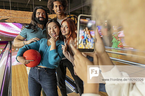 Young woman taking photo of friends through mobile phone in bowling alley