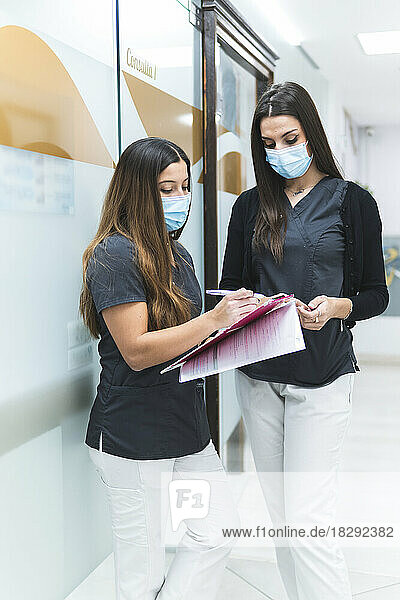 Dental assistants discussing over documents standing at clinic