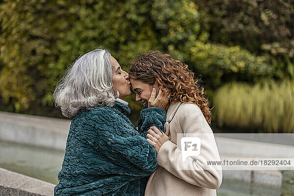 Grandmother kissing and embracing granddaughter in park