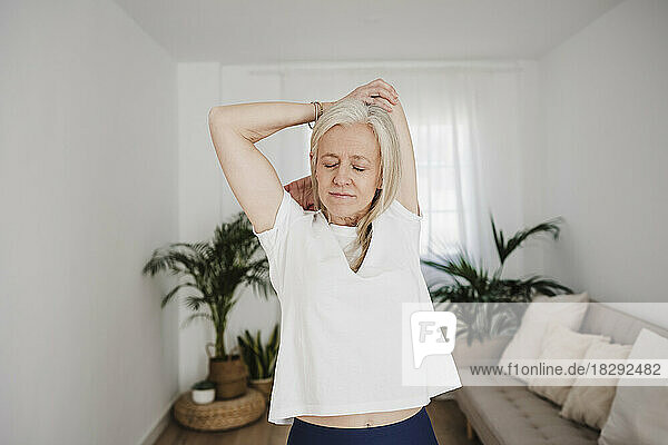 Mature woman stretching arms and exercising at home