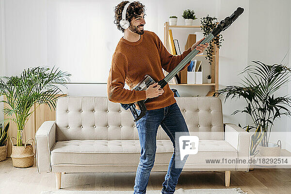 Happy young man dancing and playing guitar with vacuum cleaner at home