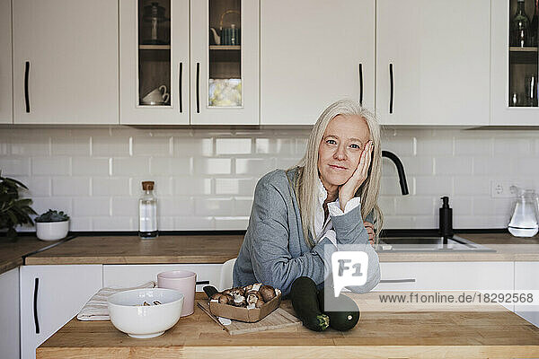 Smiling mature woman leaning on table in kitchen at home