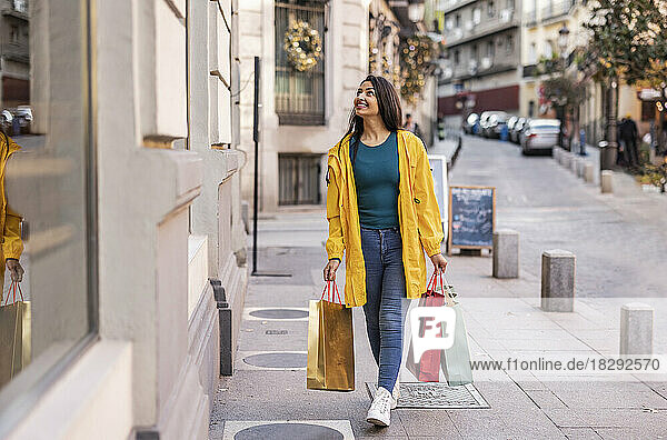 Happy young woman walking with shopping bags on footpath
