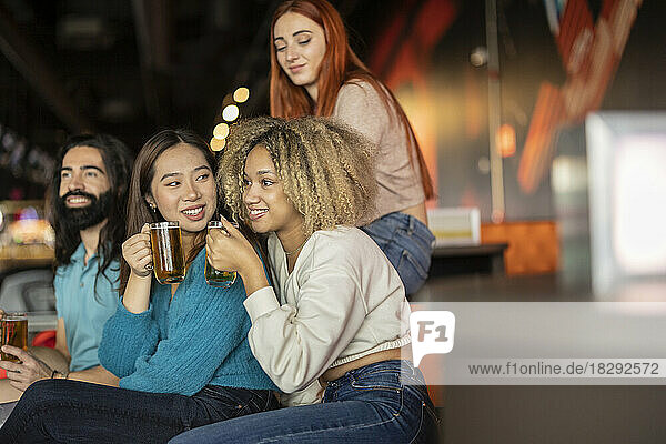Multiracial friends sitting with beer in bowling alley