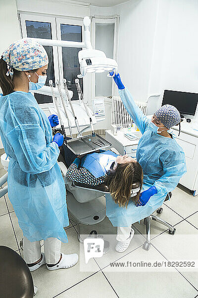 Young dentist and assistant examining patient through equipment at clinic