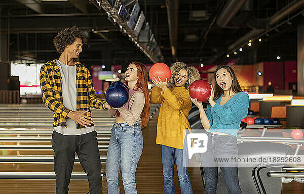 Glücklicher Mann und Frauen mit Bällen  die sich auf der Bowlingbahn vergnügen