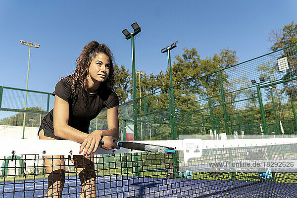 Young woman with racket leaning on tennis net