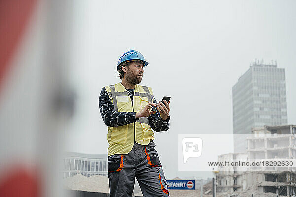 Smiling mature worker with smart phone at construction site