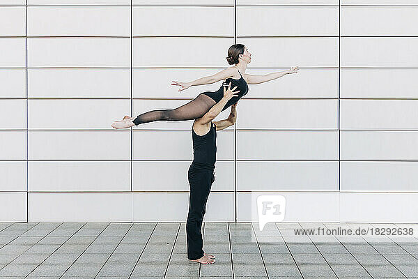 Man lifting woman practicing ballet dance in front of wall