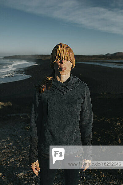 Woman covering eyes with knit hat and sticking out tongue at Janubio Beach  Lanzarote  Canary Islands  Spain