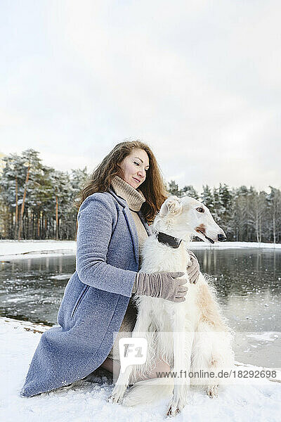 Woman stroking greyhound dog in front of frozen lake