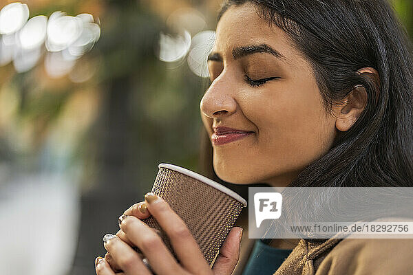 Smiling woman with eyes closed holding disposable coffee cup