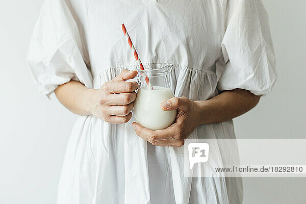 Woman holding jar of milkshake with straw in front of wall