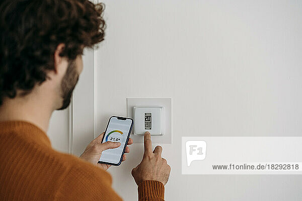 Young man operating thermostat with smart phone at home