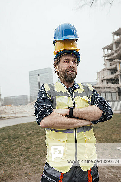 Worker standing with stack of hardhats on head at construction site