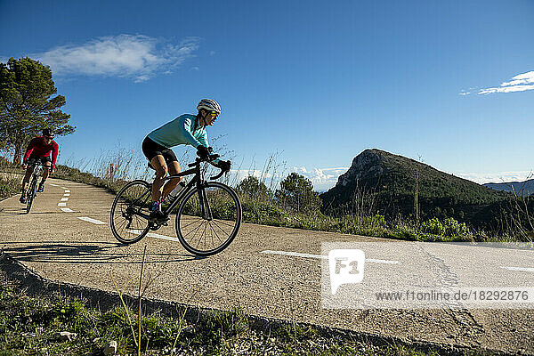 Cyclists riding bicycle on road under sky in sunlight