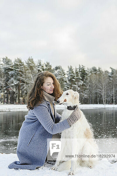 Mature woman stroking greyhound dog in front of frozen lake