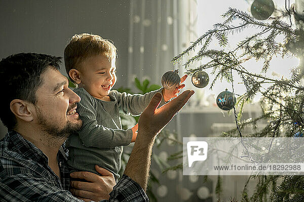 Glücklicher Vater und Sohn schmücken zu Hause den Weihnachtsbaum