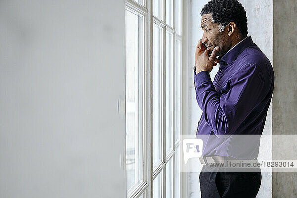 Mature businessman talking on mobile phone and looking out through window
