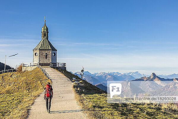 Germany  Bavaria  Female hiker walking toward Heilig Kreuz chapel standing on summit of Wallberg mountain