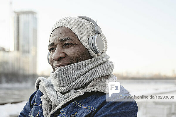 Smiling man wearing warm clothing enjoying music through wireless headphones