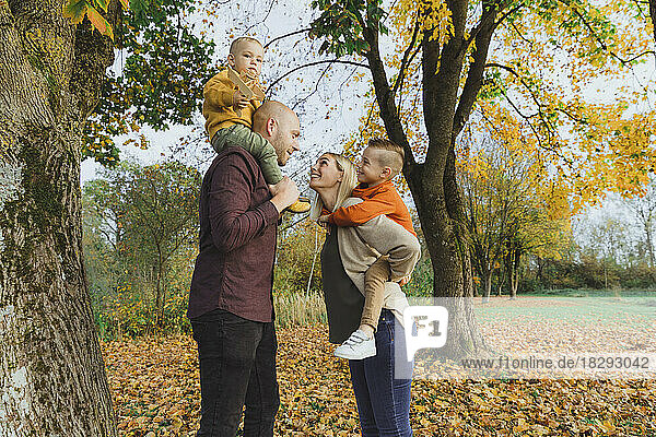 Lächelnde Frau fährt Huckepack mit Sohn und Mann  der einen Jungen auf Schultern im Herbstwald trägt