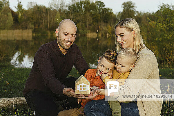 Smiling parents with children holding wooden model house in nature