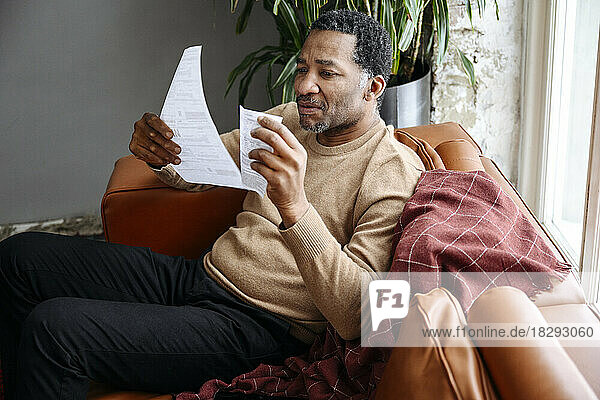Mature man examining financial bills on sofa at home