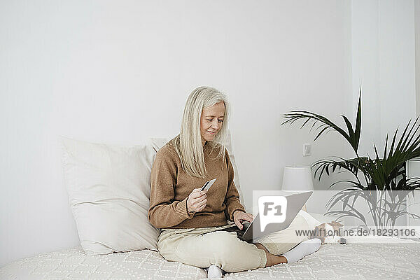 Smiling mature woman paying with credit card on laptop at home