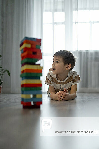Boy lying on floor with stack of toy blocks at home