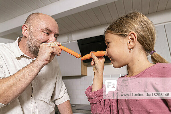 Father and daughter having fun with carrots in kitchen at home
