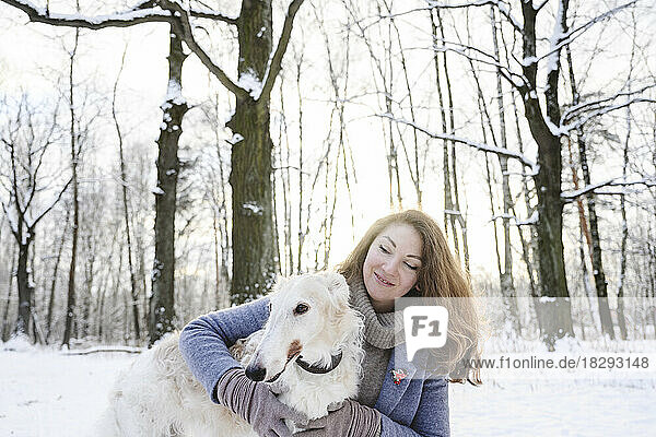 Smiling mature woman embracing greyhound dog in winter park